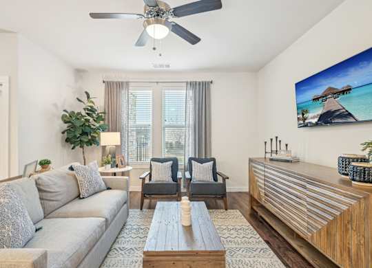 A living room with a grey couch, a wooden coffee table, and a flat screen TV mounted on the wall.