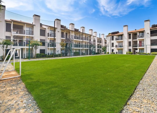 a grassy area with a swing set in front of an apartment complex