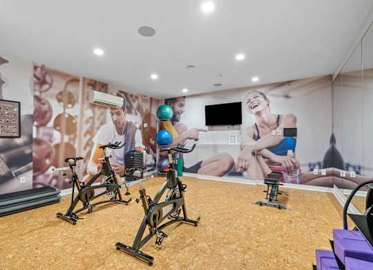 A gym with exercise bikes and a wall mural of people exercising.