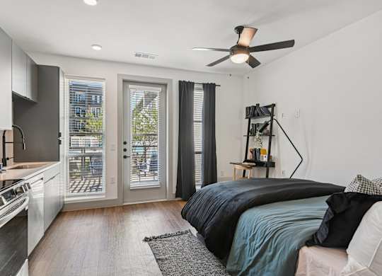 A modern bedroom with a large bed and a kitchen area in the background.