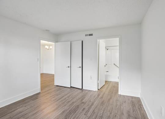 A room with white walls and wood flooring with three white closet doors.