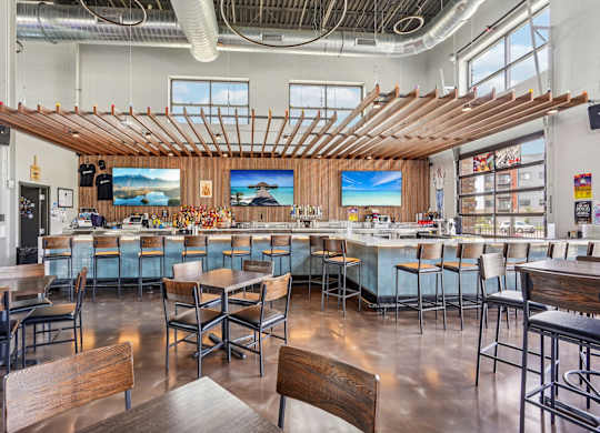 A modern restaurant with wooden tables and chairs and a bar area.