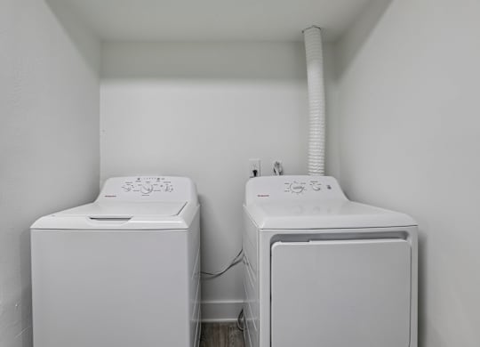 Two white washing machines in a small white room.