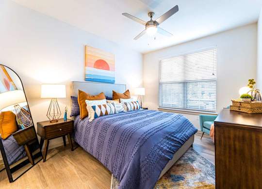 A bedroom with a bed, a chair, a nightstand, and a ceiling fan.