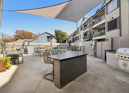 A patio with a bar and chairs under a shade sail.