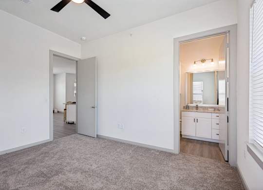 A room with a ceiling fan and a bathroom visible through an open door.