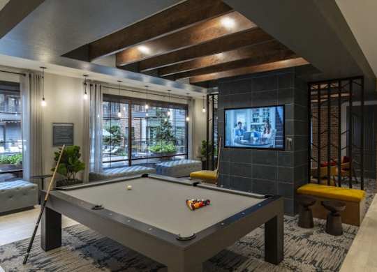A pool table is in the middle of a room with a brick wall and a television.