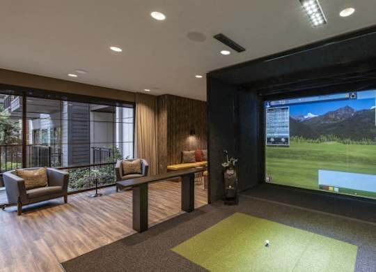 A room with a golf simulator screen and a green carpet.