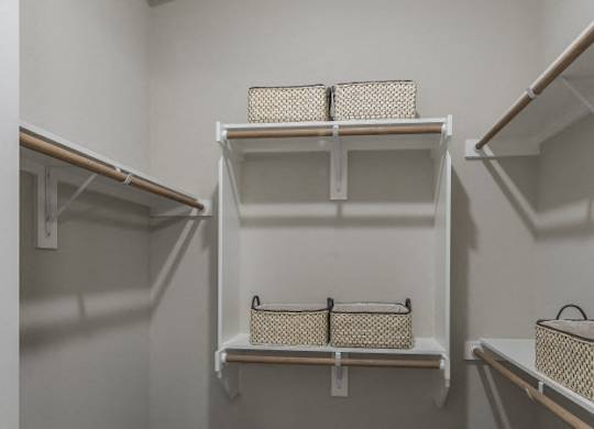 A white closet with three shelves and baskets on them.