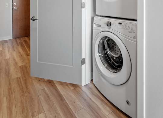 A white washing machine is in a cabinet in a room with wooden floors.