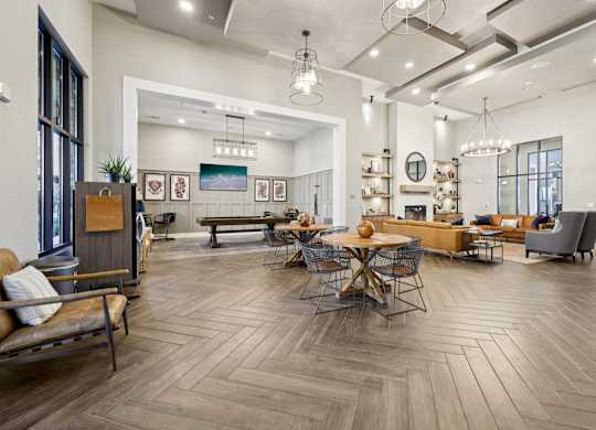 Large open-concept lobby featuring a social lounge and gaming zone, furnished with modern tables and accented by black industrial light fixtures.
