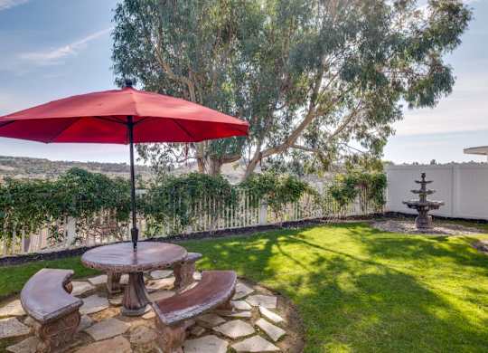 A red umbrella is on a patio table with a stone bench.