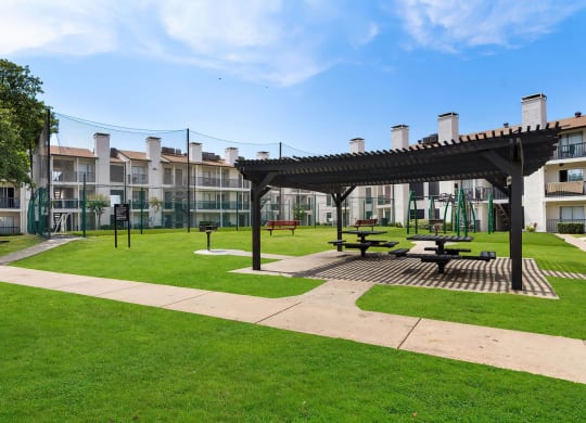 a pergola sits in the middle of a grassy area in front of an apartment