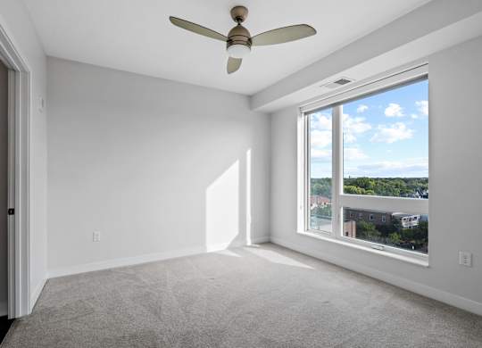 A room with a ceiling fan and a large window overlooking a cityscape.