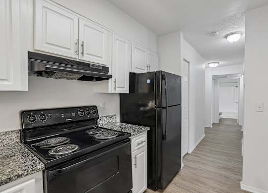 A black refrigerator sits in a kitchen with white cabinets.