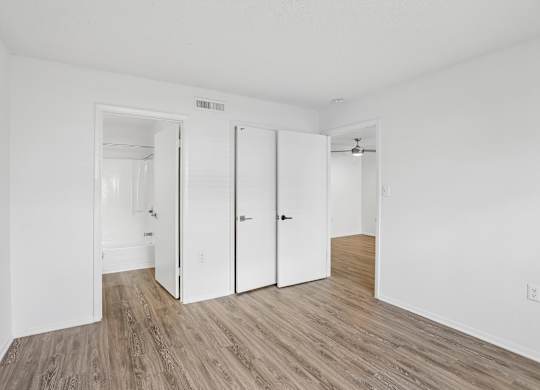 A room with white walls and wood flooring with three doors.