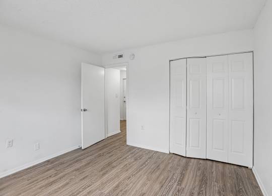 A room with white walls and a wooden floor with a white door and a white wardrobe.