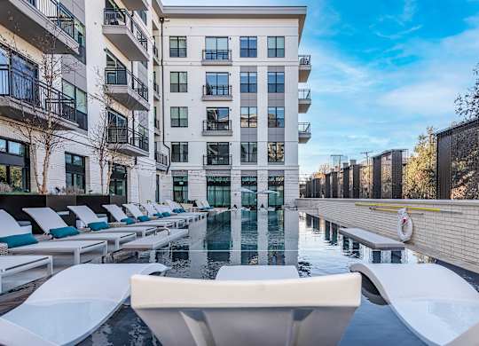 A large white pool with lounge chairs is in front of a tall building.
