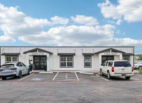 A white building with a sign that says "Fitness Center" is in front of a blue sky with clouds.