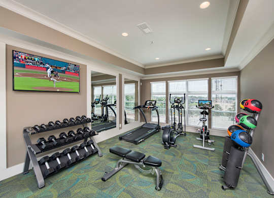 A well equipped gym with a television screen showing a baseball game.