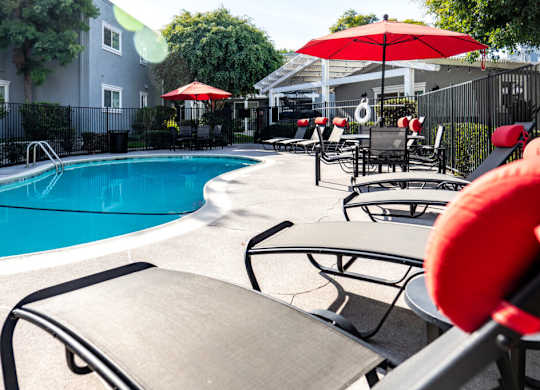 A pool area with red umbrellas and lounge chairs.