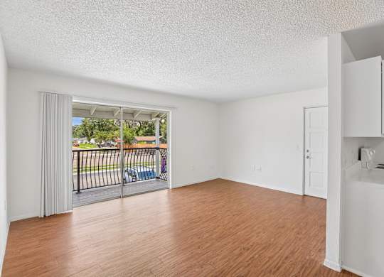 A room with wooden floors and white walls, with a balcony visible through the door.