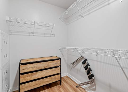 A white closet with a wooden chest of drawers and a metal rack.