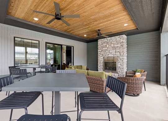 A modern outdoor dining area with a stone fireplace and a ceiling fan.
