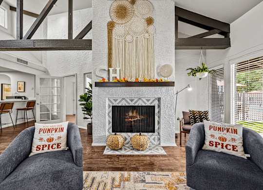 A living room with a fireplace and two grey armchairs with pillows that say pumpkin spice.