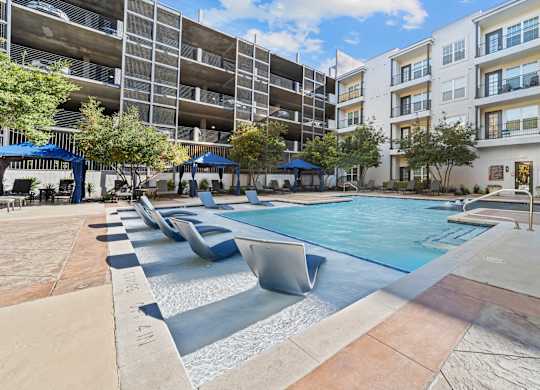an apartment pool with lounge chairs in front of an apartment building