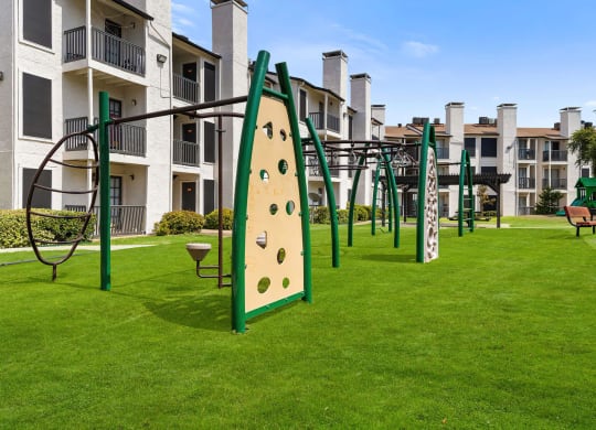 a playground with a climbing wall and monkey bars in front of an apartment building