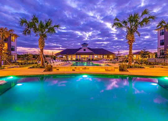 A pool surrounded by palm trees and buildings at dusk.
