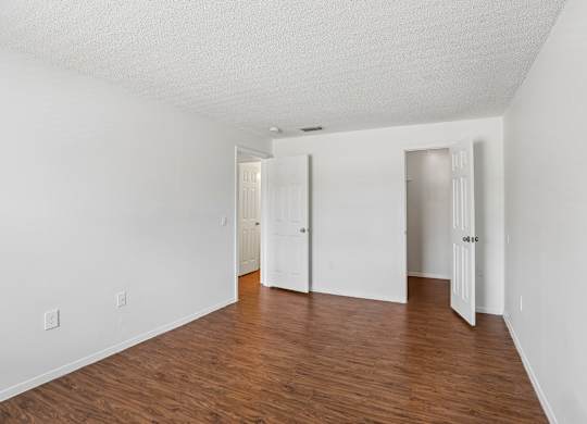 A room with white walls and wood flooring with three doors.