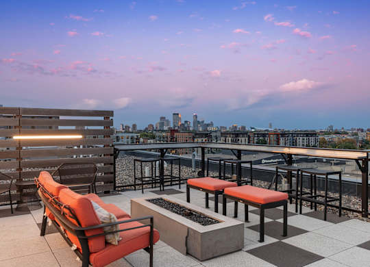 A rooftop patio with a bench, chairs, and a table.