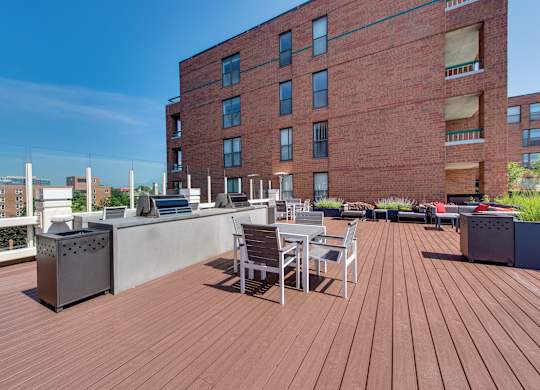A wooden rooftop deck grilling stations surrounded by metal tables and chairs.