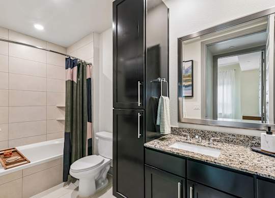 A bathroom with a black cabinet, a white toilet, a bathtub with a towel, and a mirror.