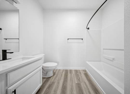 A white bathroom with a toilet, sink, and wood flooring.