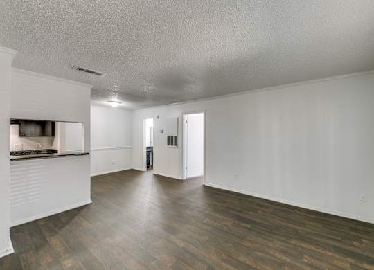 an empty living room and kitchen with wood flooring and white walls