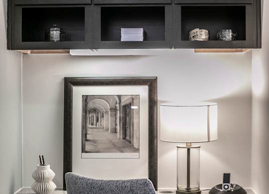 A grey chair is in front of a desk with a lamp and a picture frame.