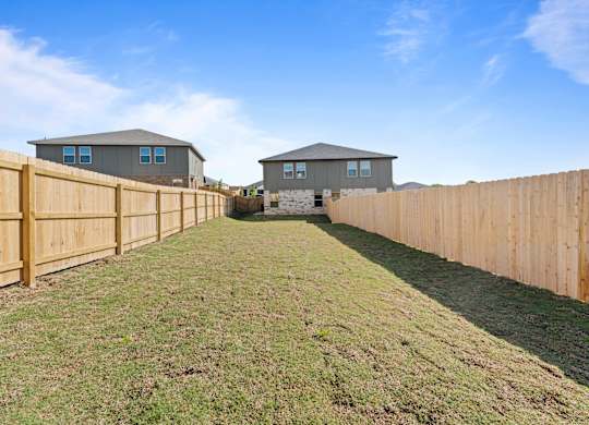 a backyard with a wooden fence and two houses in the background
