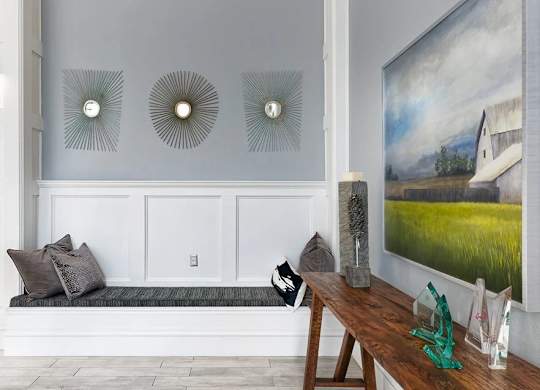 A room with a bench, a table, and three wall decorations.