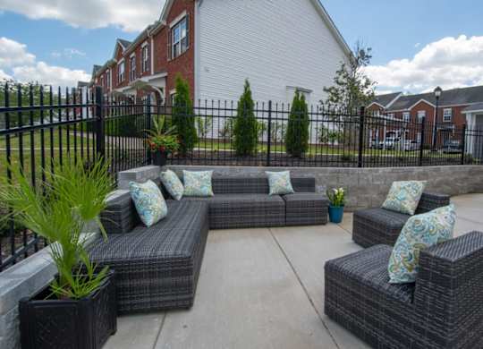 A patio with a black fence and grey wicker furniture.