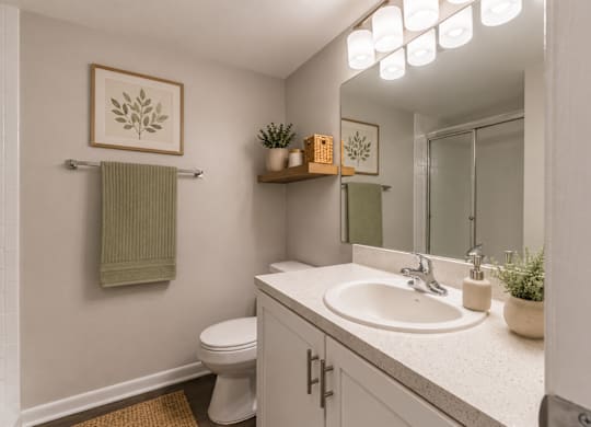 A bathroom with a toilet, sink, mirror, and a green towel hanging on the wall.