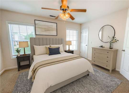 A bedroom with a large bed, a ceiling fan, and a nightstand with a lamp.