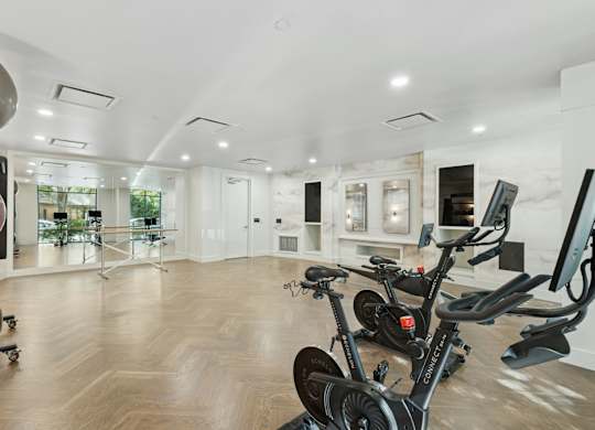 A room with a wooden floor and a row of stationary bikes.