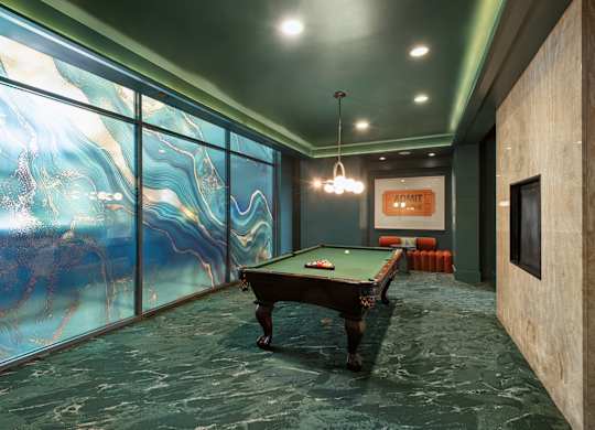 A pool table in a room with a green floor and a glass wall.