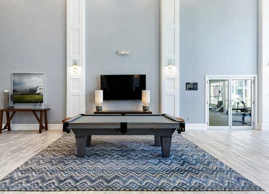 A pool table in the middle of a room with a television and a painting on the wall.