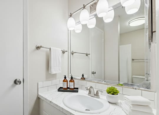 A white bathroom with a sink, mirror, and lights.
