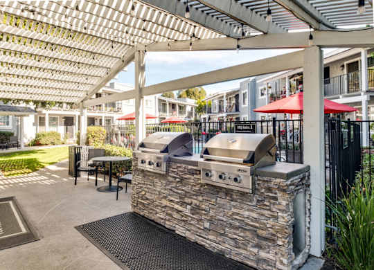 A barbecue grill is located under a white pergola.