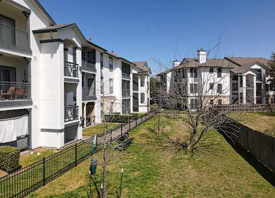 A row of white apartment buildings with black fences and green bushes.